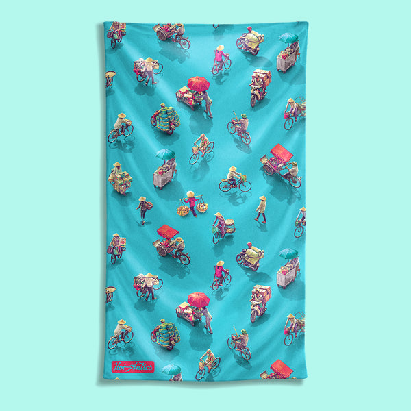 Front view of a large blue beach towel with a pattern of people on bicycles and motorcycles, featuring Hoi-Antics brand logo.