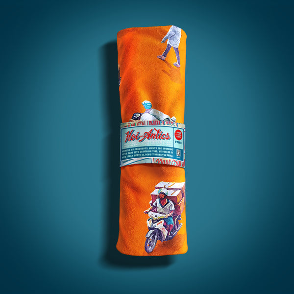 Front view of a rolled up large orange beach towel with a pattern of people on bicycles and motorcycles, featuring Hoi-Antics brand wrapper.