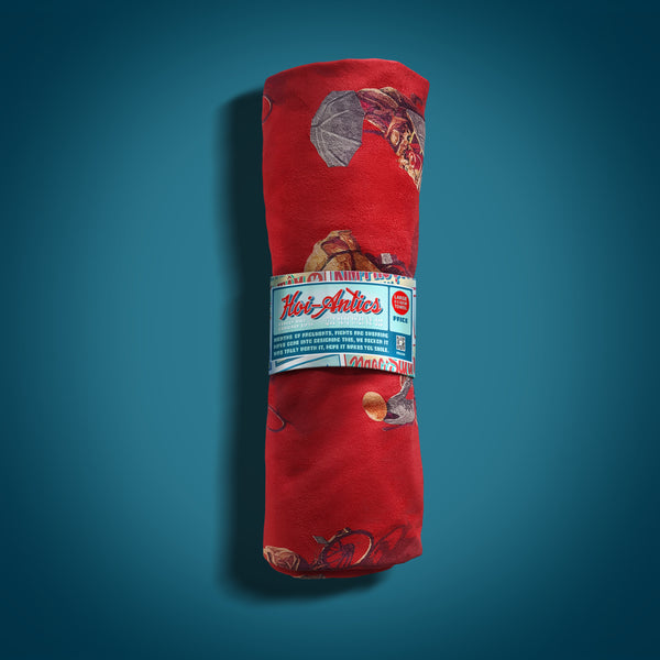 Front view of a rolled up large red beach towel with a pattern of people on bicycles and motorcycles, featuring Hoi-Antics brand wrapper.