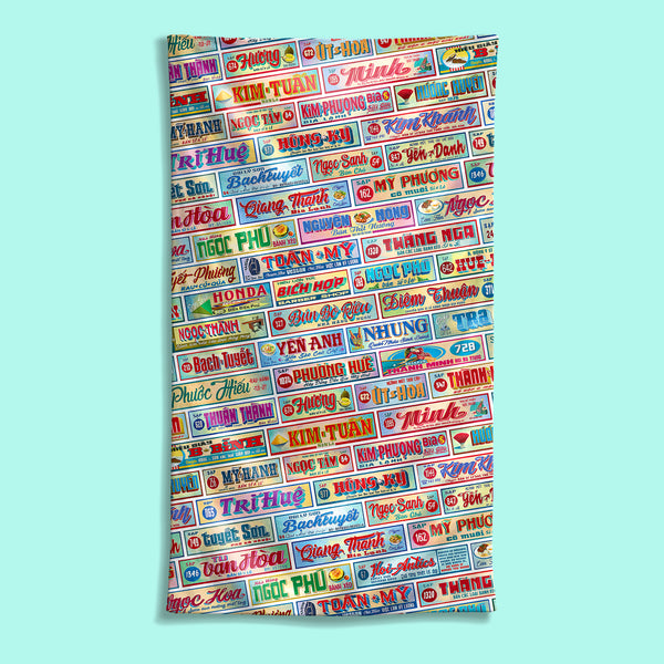Front view of a large Shop Signs beach towel with a Vietnamese Shop Signage pattern, featuring Hoi-Antics brand logo.