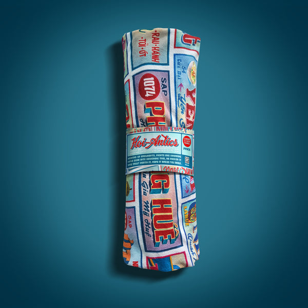 Front view of a rolled up large Shop Sign beach towel with a Vietnamese Shop Signage pattern, featuring Hoi-Antics brand wrapper.