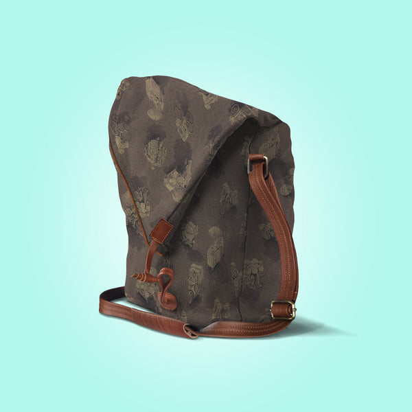 Three quarter view of a closed antique umber canvas and brown leather bag with a pattern of people on bicycles and motorcycles, featuring Hoi-Antics brand logo.