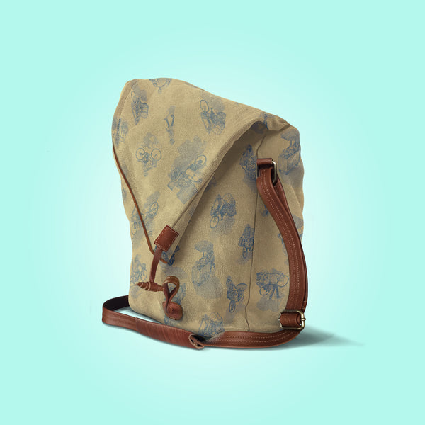 Three quarter view of a closed antique yellow canvas and brown leather bag with a pattern of people on bicycles and motorcycles, featuring Hoi-Antics brand logo.