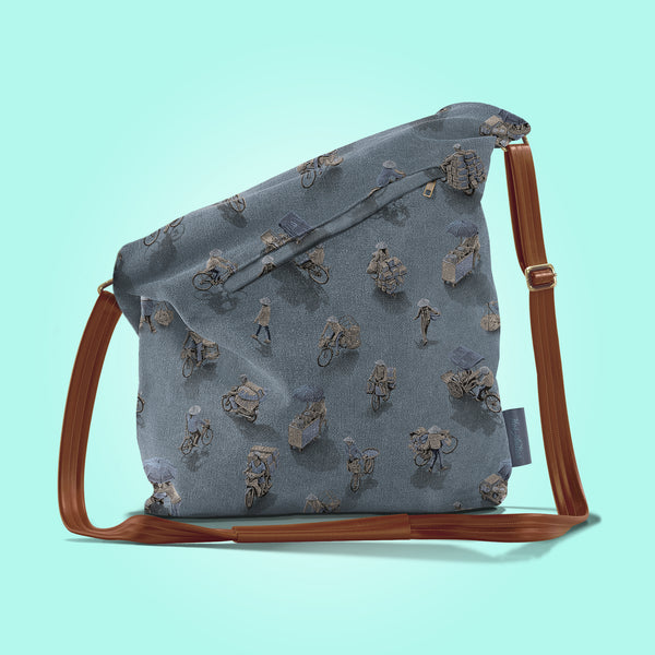 Back view of a closed moonlit grey canvas and brown leather bag with a pattern of people on bicycles and motorcycles, featuring Hoi-Antics brand logo.