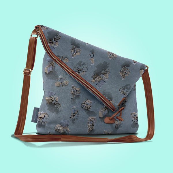Front view of a closed moonlit grey canvas and brown leather bag with a pattern of people on bicycles and motorcycles, featuring Hoi-Antics brand logo.