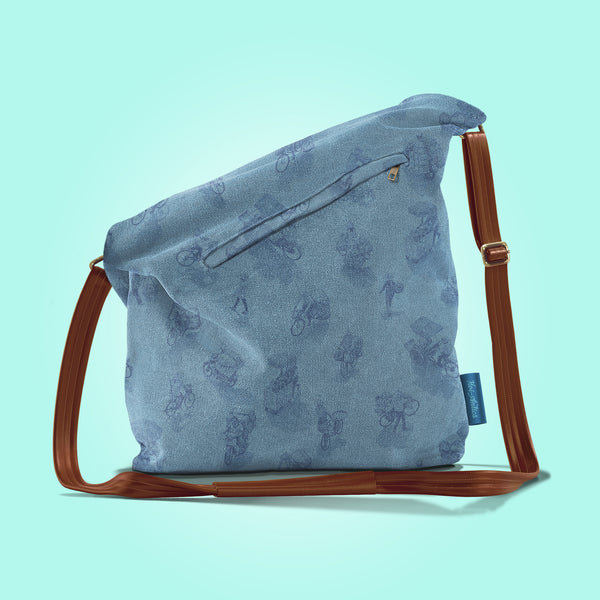 Back view of a closed pastel blue canvas and brown leather bag with a pattern of people on bicycles and motorcycles, featuring Hoi-Antics brand logo.