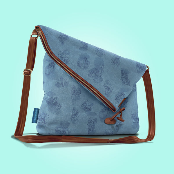 Front view of a closed pastel blue canvas and brown leather bag with a pattern of people on bicycles and motorcycles, featuring Hoi-Antics brand logo.