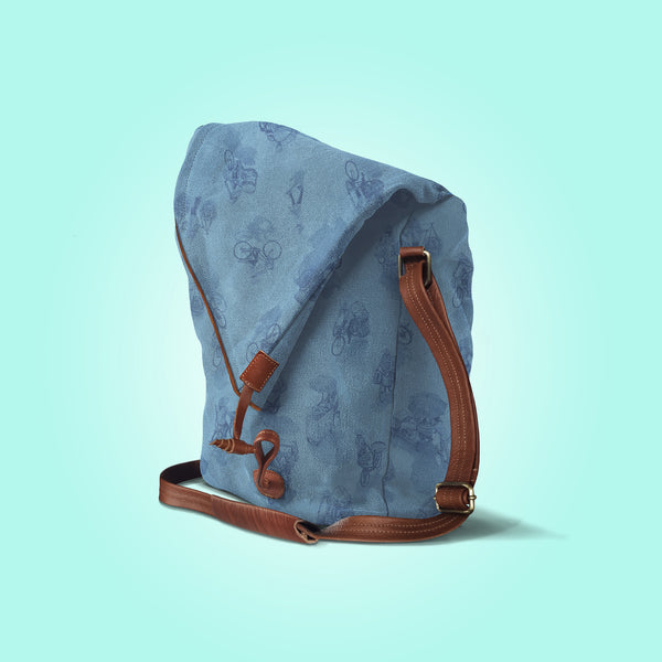 Three quarter view of a closed pastel blue canvas and brown leather bag with a pattern of people on bicycles and motorcycles, featuring Hoi-Antics brand logo.