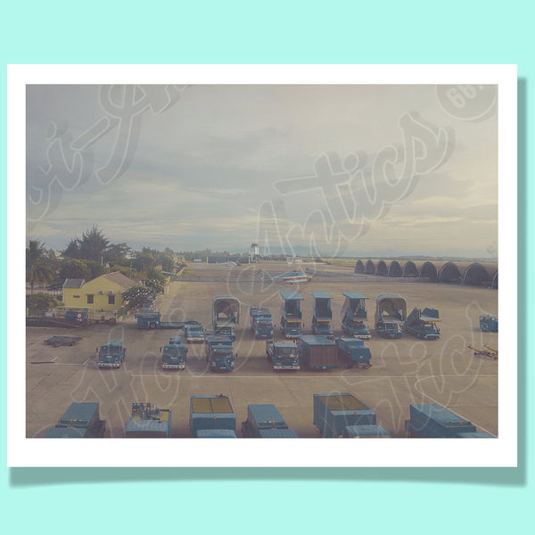 Front view of a Vietnamese airport setting, printed on fine art paper, including helicopters, ground vehicles, buildings, hangers and a hazy afternoon sky.