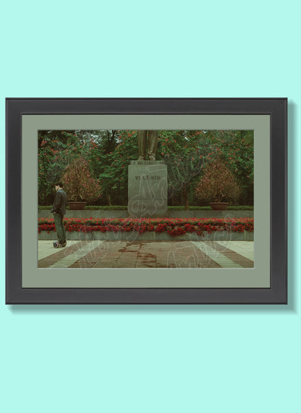 Front view of a Vietnamese day scene, printed on fine art paper, framed and including a statue of Lenin and a Vietnamese man riding a self-balancing scooter.