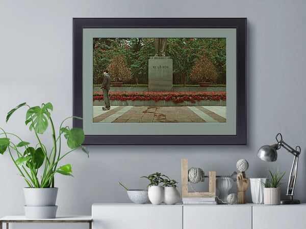 A Vietnamese day scene, printed on fine art paper, framed and hanging on a lounge wall, including a statue of Lenin and a Vietnamese man riding a self-balancing scooter.