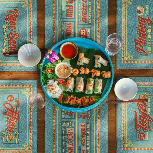 Distinct Vietnamese table mats and runner, printed on canvas fabric, featuring Vietnamese shop sign artwork, borders and patterns, with Vietnamese food and drinks